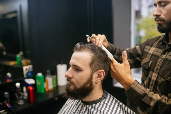 Alegre joven barbudo conseguir corte de pelo por peluquería en la barbería —  Fotos de Stock