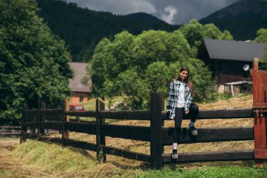 Çitin üzerinde oturan genç ve çekici beyaz bir kadın.
