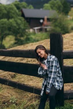 Genç, çekici, beyaz bir kadın çitin yanında duruyor.