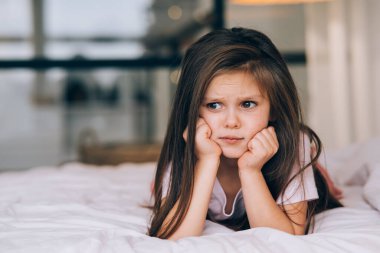 Yatağa uzanmış üzgün yüzlü tatlı küçük kız.