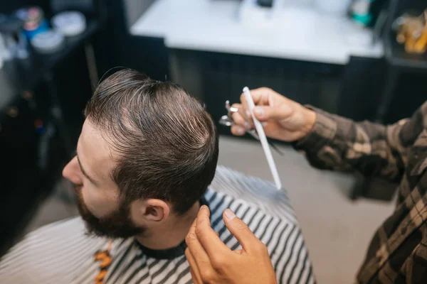 Pria muda berjenggot ceria mendapatkan potongan rambut oleh penata rambut di salon — Stok Foto