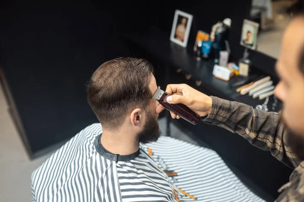 Maestro en barbería hace mens corte de pelo con cortador de pelo —  Fotos de Stock