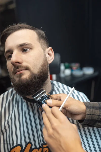 Peluquero trabaja con un cortador de barba. Hipster cliente conseguir corte de pelo. — Foto de Stock