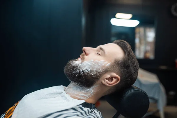 Homem com espuma de barbear no rosto em uma barbearia — Fotografia de Stock