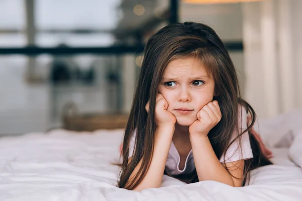 Roztomilá holčička se smutnou tváří ležící na posteli — Stock fotografie