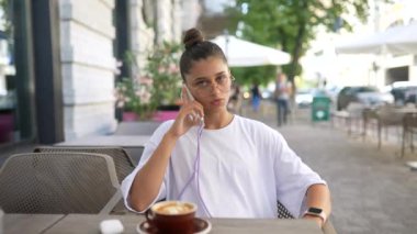 Güzel genç bir kadın sokak kafesinde oturmuş akıllı bir telefonla konuşuyor.