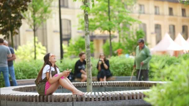 Mujer bastante joven utilizando la aplicación de teléfono móvil en el parque de la ciudad — Vídeos de Stock