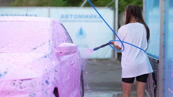 Brunette van een hogedrukslang brengt een reiniger aan op de auto — Stockvideo