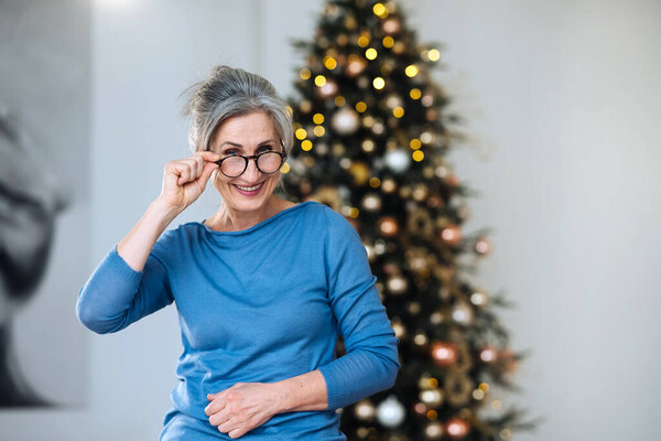 Elderly lady smiling and looking in camera, Xmas tree on background Royalty Free Stock Photos