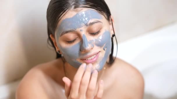 Soins de la peau. Jeune femme appliquant un masque vert argile sur son visage. — Video