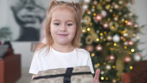 Очаровательная маленькая девочка держит подарок на фоне рождественских елок — стоковое видео