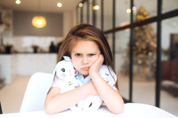 Pequena Menina Triste Abraçando Brinquedo Favorito Enquanto Sentado Mesa Infância — Fotografia de Stock