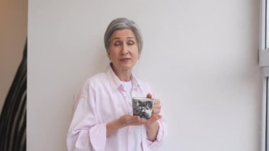 Rastgele giyinmiş yaşlı bir kadının portresi izole edilmiş beyaz bir arka planda elinde bir kupa tutuyordu. Duygusal yüz..