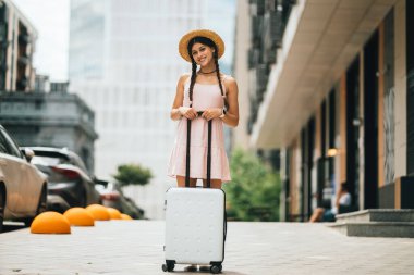 Modern bir şehrin arka planında bavulu olan güzel bir kadın.