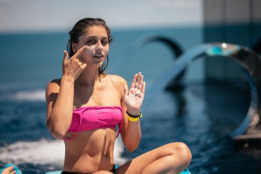 Portrait photo of smiling woman is applying sunscreen on her face.
