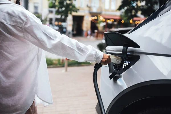 Human hand is holding Electric Car Charging nozzle. Selective focus on hand and nozzle