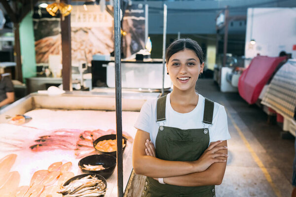Smiling female fishmonger standing near seafood shop counter