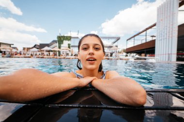 Güzel genç bir kadın yüzme havuzunun kenarında dinleniyor.