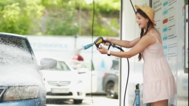 Yüksek basınçlı hortumdan çıkan güzel bir kadın arabasına sabun köpüğü sürüyor. otomatik temizleme konsepti