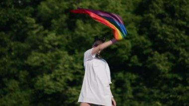 Igbt gurur bayrağı taşıyan genç bir kadın parkta yürüyor..