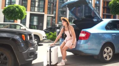 Genç mutlu kadın bavulunu arabanın bagajına koyuyor. Tatil kavramı.