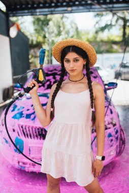 Genç kadın yüksek basınçlı hortum pembe köpükle kaplı bir arabanın önünde duruyor.