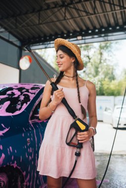 Yüksek basınçlı hortumlu genç kadın pembe köpükle kaplı arabanın yanında duruyor.