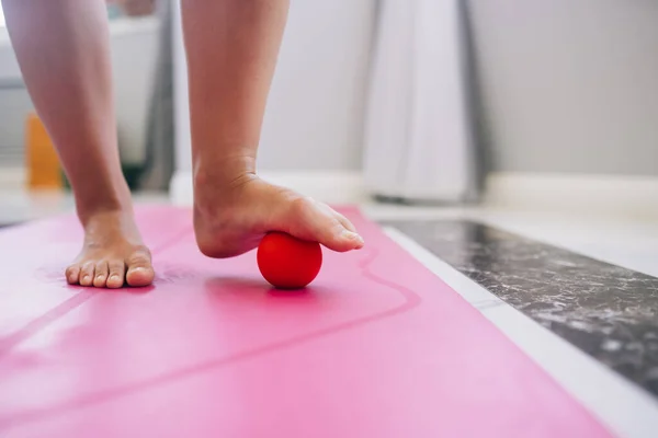 Woman massages the foot with a ball. The ball will apply pressure to the painful spot and raise the procedure