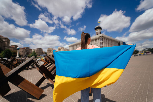A young woman carries the flag of Ukraine fluttering behind her in the street