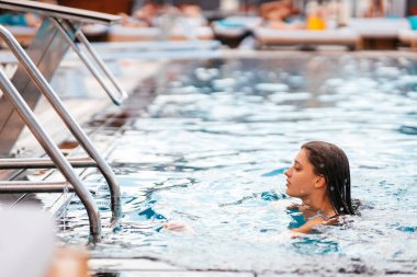 Mayo giymiş genç bir kadın havuzdan çıkmak için merdivene tırmanıyor.