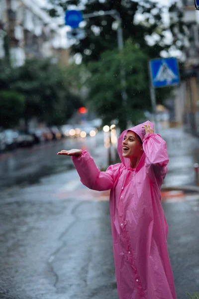 Young smiling woman with a pink raincoat on the street while enjoying a walk through the city on a rainy day.