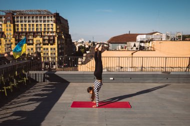 Güzel genç bir kadın dışarıda çalışıyor ve yoga minderi üzerinde yoga amuda kalkıyor.