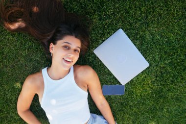 Yeşil çim parkında yatan çekici genç bir kadın. Serbest çalışma kavramının avantajları. Arkaplan, boşluğu kopyala