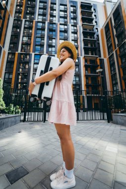 Genç ve güzel bir kadın modern bir evin önünde elinde bir bavul tutuyor.