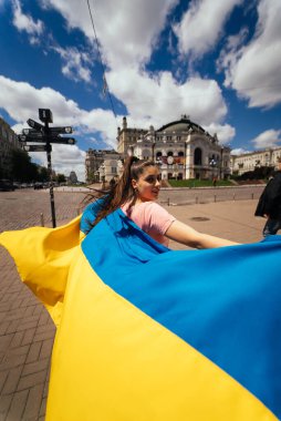 Sokakta dalgalanan Ukrayna bayrağını taşıyan genç bir kadın.