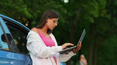 A young woman uses a laptop near a car in city center outdoors