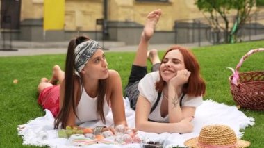 Two women having picnic together, laying on the plaid on the lawn