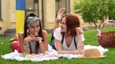 Two women having picnic together, laying on the plaid on the lawn