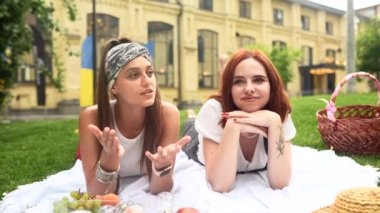 Two women having picnic together, laying on the plaid on the lawn