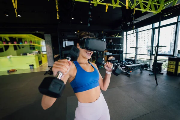 Portrait view of the woman wearing glasses of the virtual reality exercising with dumbbells at gym.