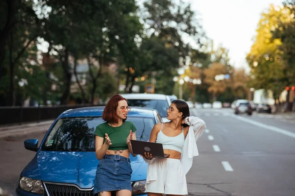 两个年轻女子在路上的汽车旁边带着笔记本电脑 — 图库照片