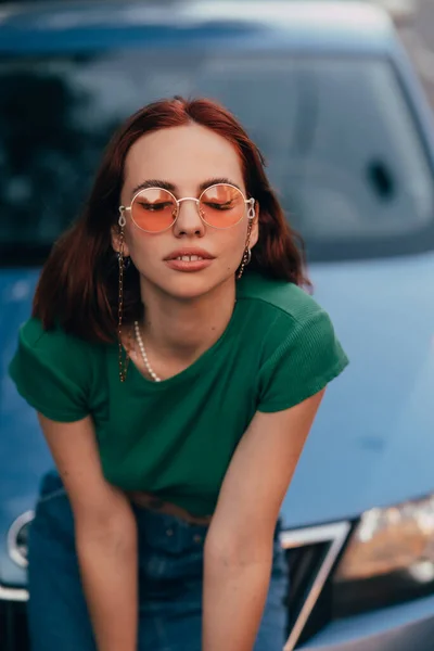 Piękna Dziewczyna Okularach Przeciwsłonecznych Siedzi Masce Niebieskiego Samochodu Drodze — Zdjęcie stockowe