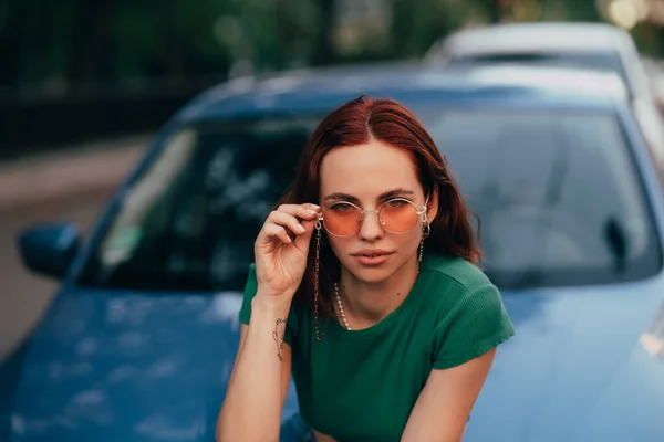 Menina Bonita Óculos Sol Senta Capô Carro Azul Contra Estrada — Fotografia de Stock