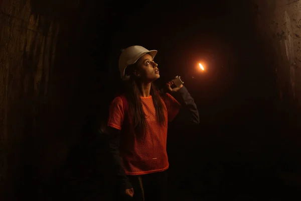 一个拿着手电筒的年轻女挖掘机探索隧道 — 图库照片