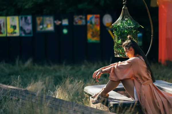 Mutlu esmer kadının yan görüntüsü bankta oturuyor ve günbatımının tadını çıkarıyor.