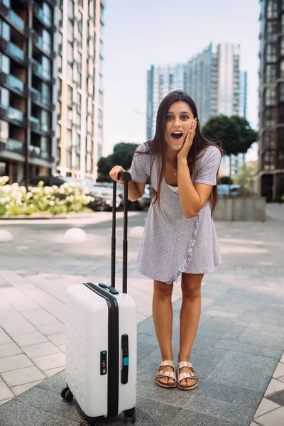 Stylish woman with suitcase looking at camera at the street