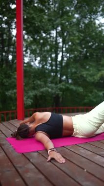 Genç bir kadın sabah tahta bir podyumda yoga yapıyor.