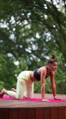 Genç bir kadın sabah tahta bir podyumda yoga yapıyor.