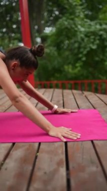 Genç bir kadın sabah tahta bir podyumda yoga yapıyor.