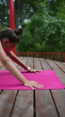 Genç bir kadın sabah tahta bir podyumda yoga yapıyor.